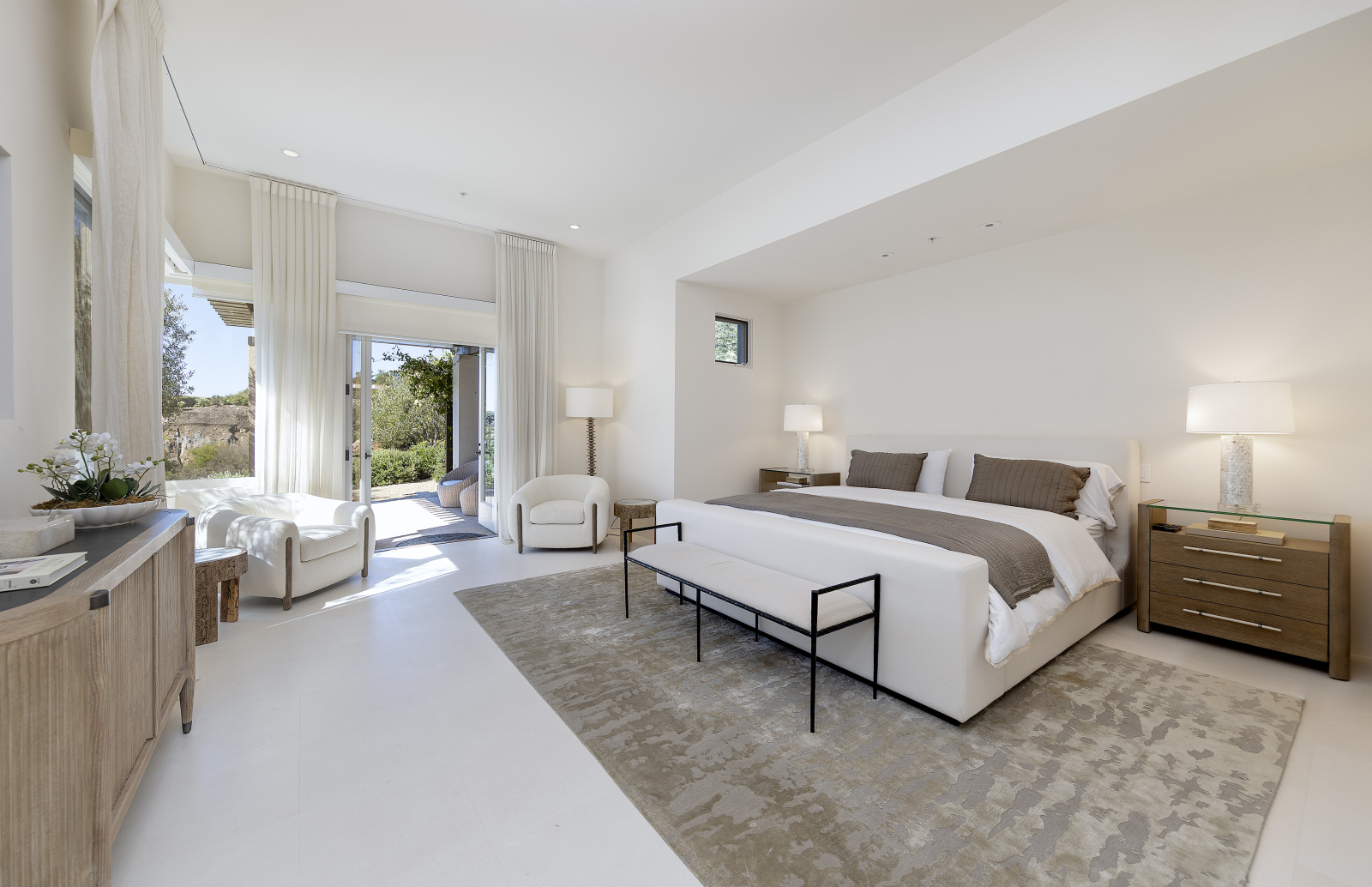 Bright primary bedroom in a Montecito luxury home with neutral décor, large windows, and doors opening to an outdoor terrace.